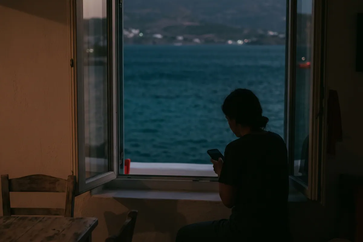 Alacakaranlıkta pencere önünde telefon kullanan uzak bir figür